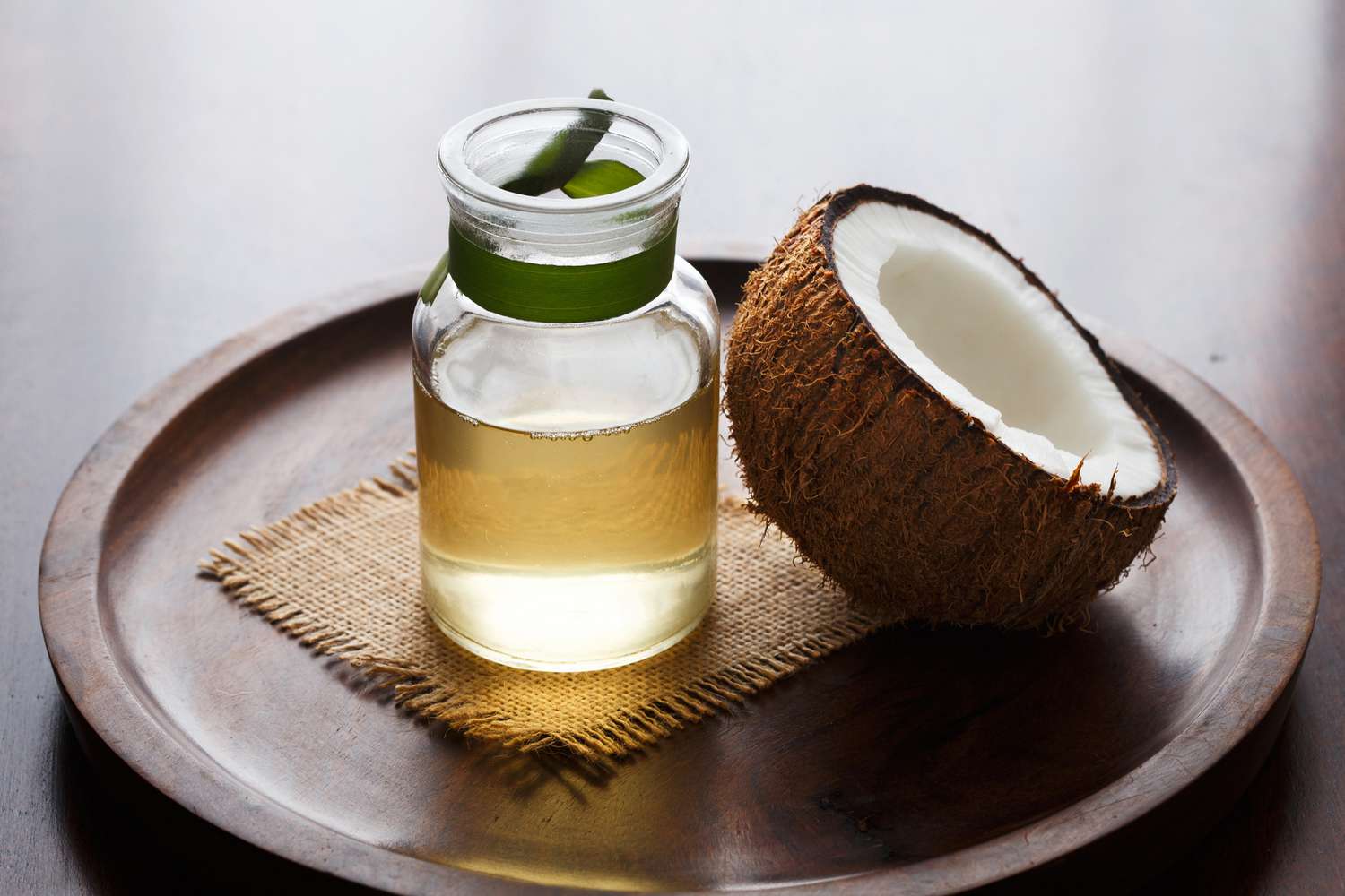 Coconut water in a glass bottle next to a halved coconut on a wooden tray.