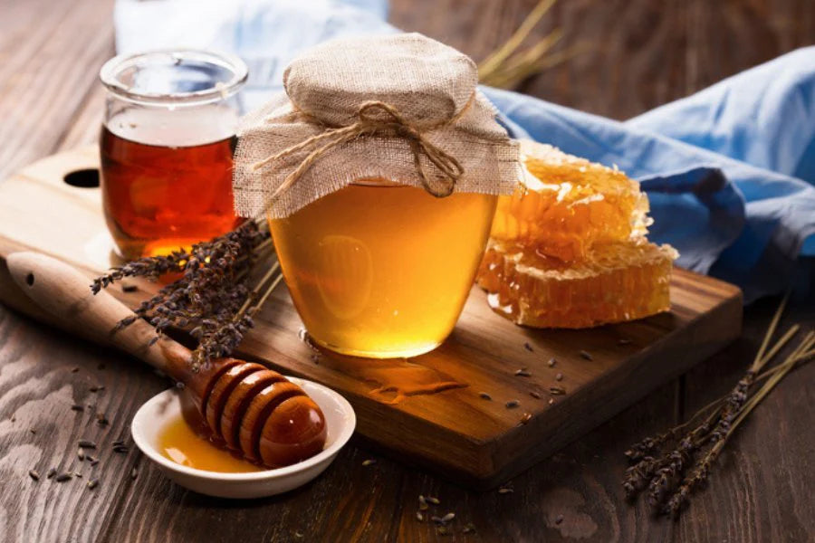 Jar of honey, honeycomb, and honey dipper on a wooden board with a blurred background